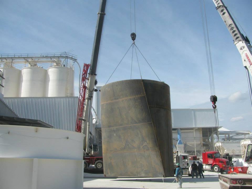 Crane lifting a large steel tank into position at an industrial plant