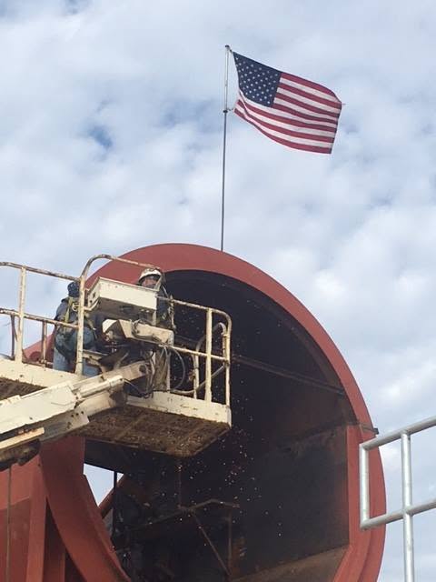 MIC Steel crew on a lift working below an American flag on an industrial structure